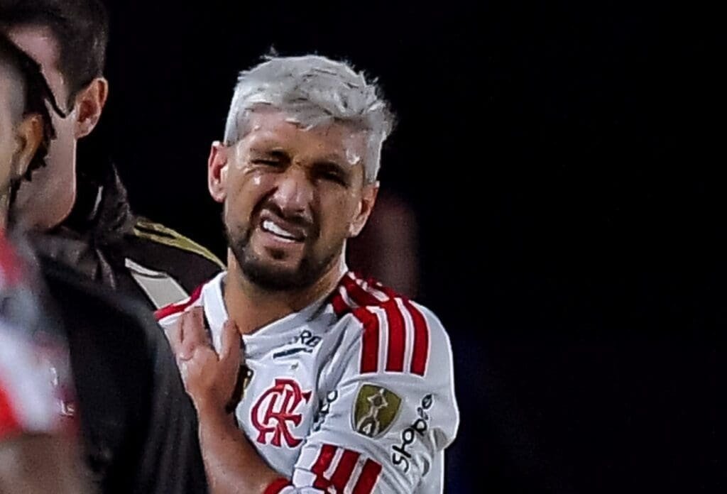 Arrascaeta com expressão de dor e mão no ombro direito durante Estudiantes x Flamengo