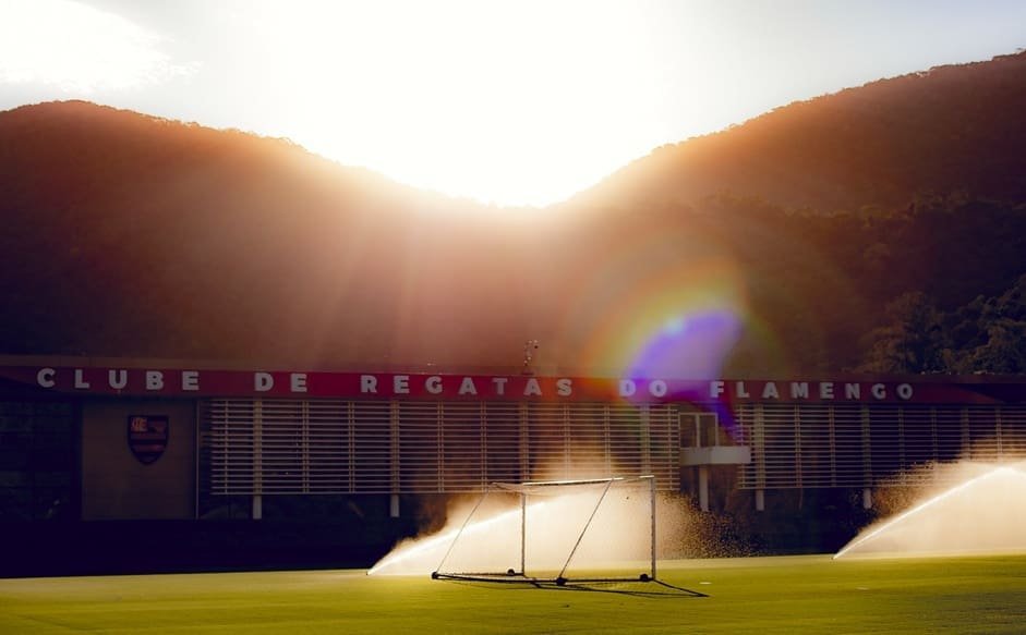Ninho do Urubu vira palco de preparação de outro clube da Libertadores Imagem do campo do Ninho do Urubu no entardecer com irrigação ligada