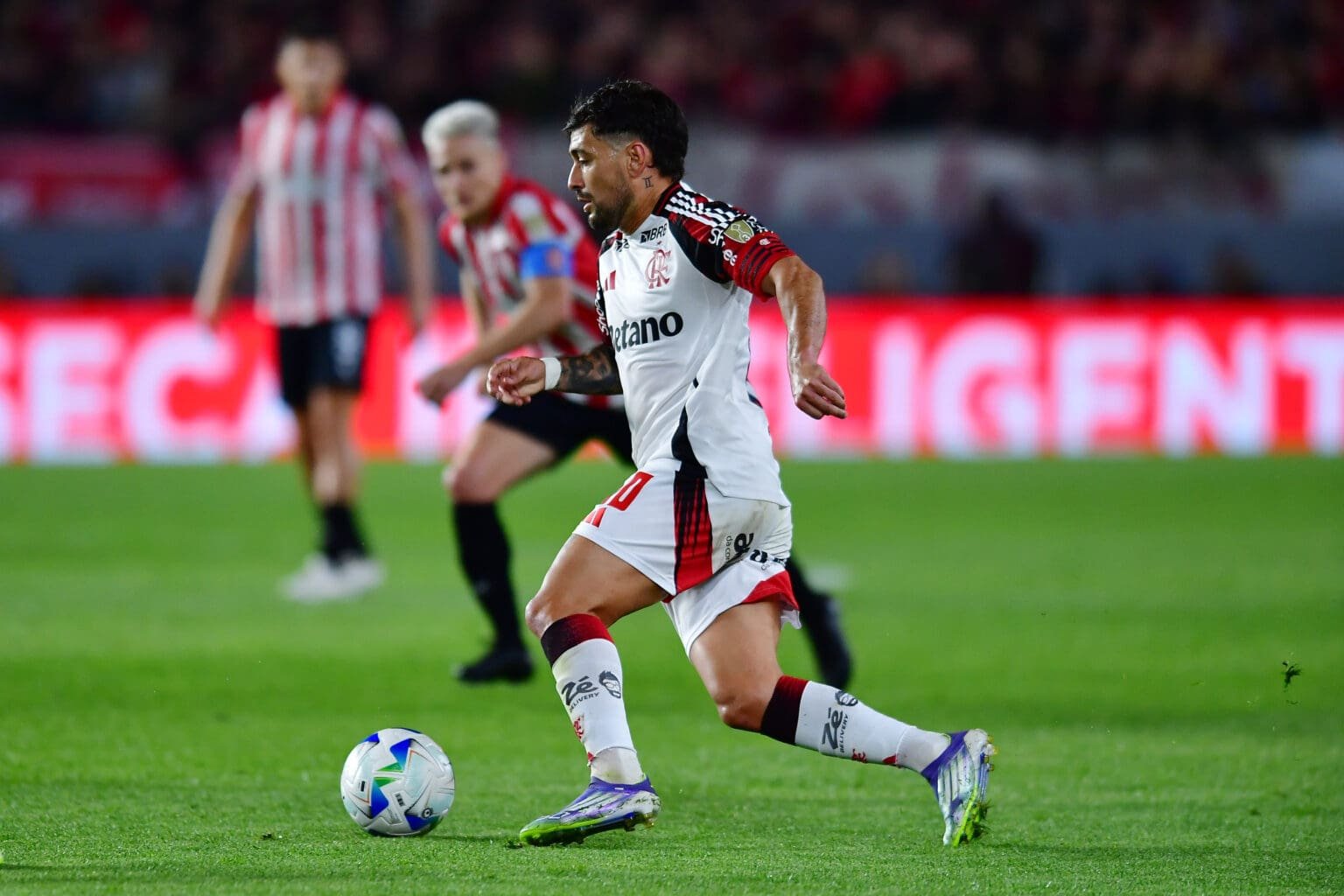 Estudiantes x Flamengo em 2025; Arrascaeta carrega bola em jogo no Estádio Uno