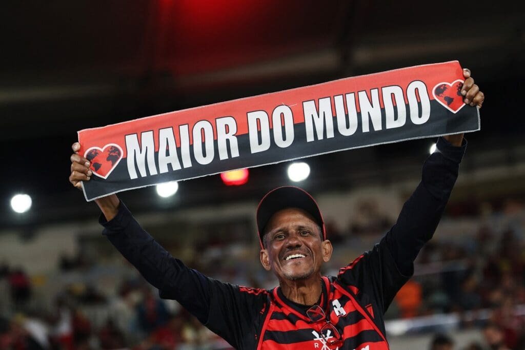 Torcedor do Flamengo sorridente segurando faixa rubro-negra escrito "maior do mundo" no Maracanã